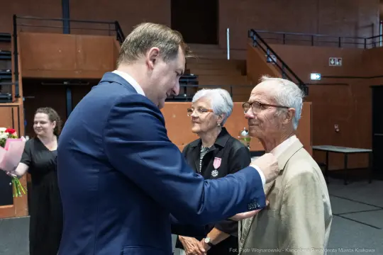 Uroczystość wręczenia odznaczeń, mężczyzna przypina medal starszemu mężczyźnie.