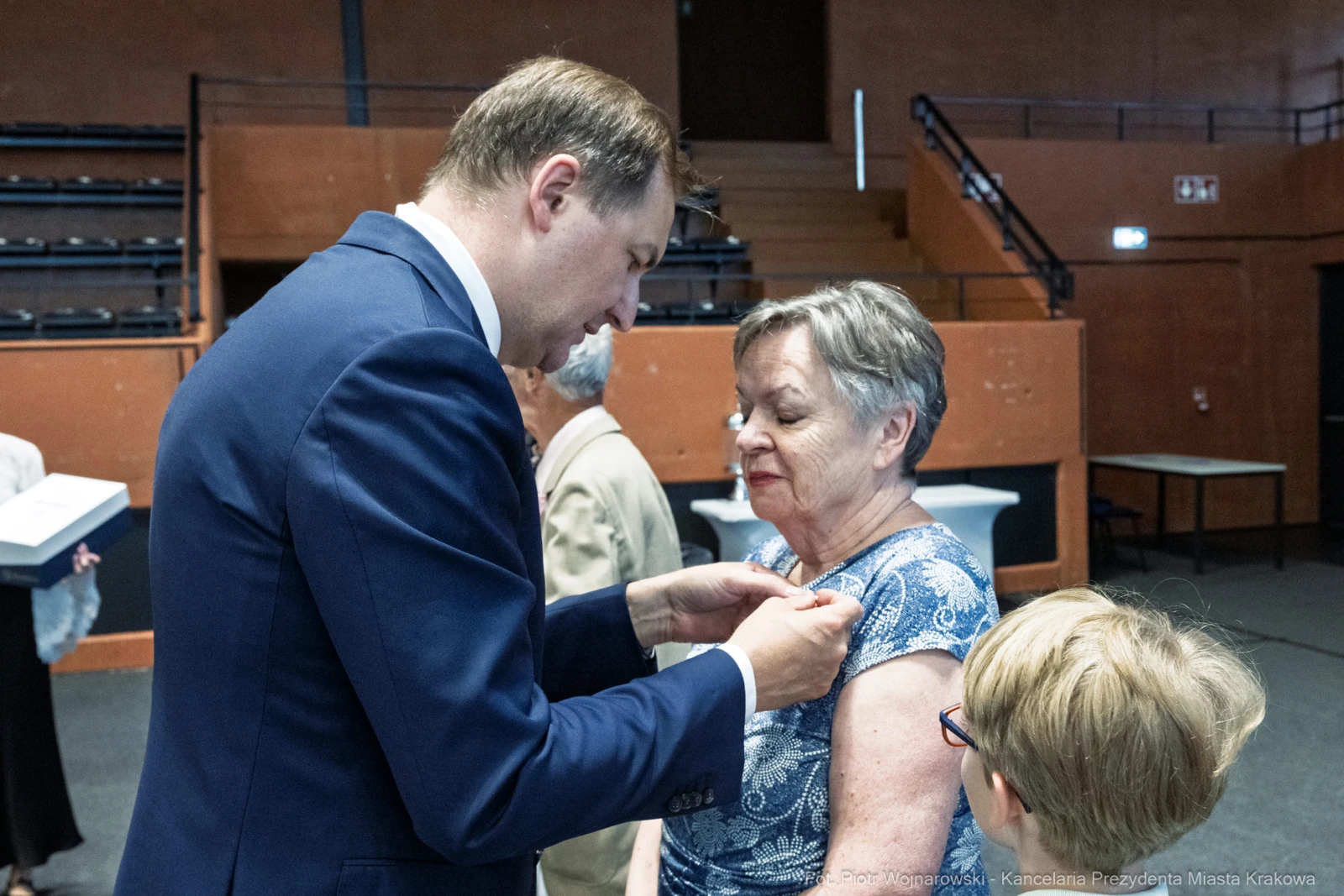 Mężczyzna przypina odznaczenie kobiecie podczas uroczystości. W tle widoczni goście.  Autor: Piotr Wojnarowski