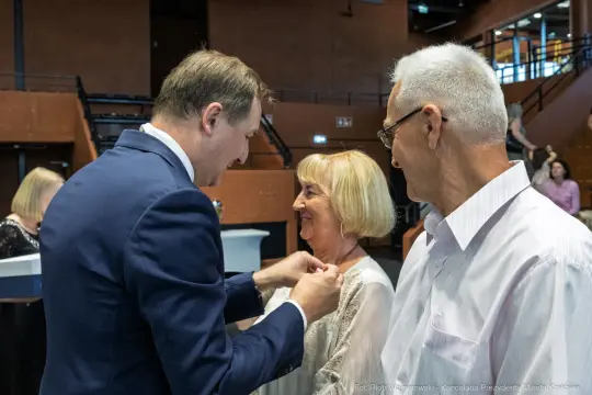 Uroczystość wręczenia odznaczeń, uśmiechnięte twarze i radosna atmosfera.