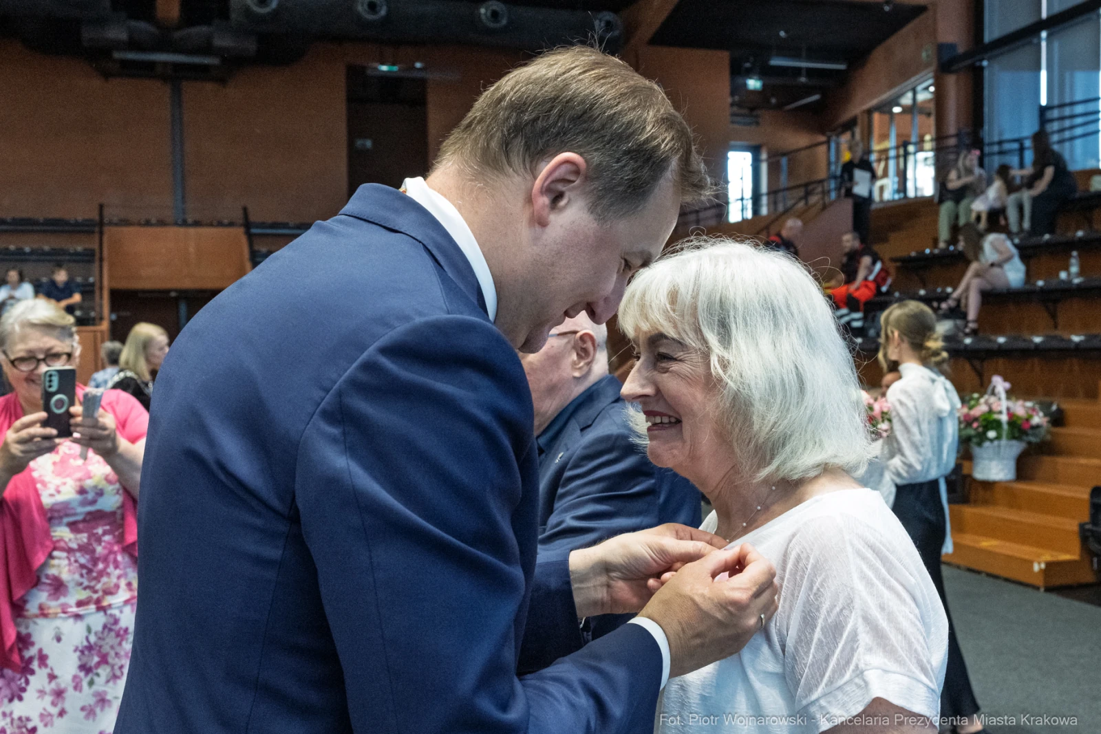 Mężczyzna przypina odznaczenie kobiecie podczas uroczystości w sali.  Autor: Piotr Wojnarowski