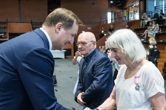 Wręczenie odznaczeń w trakcie uroczystości, uściski dłoni i uśmiechy uczestników.
