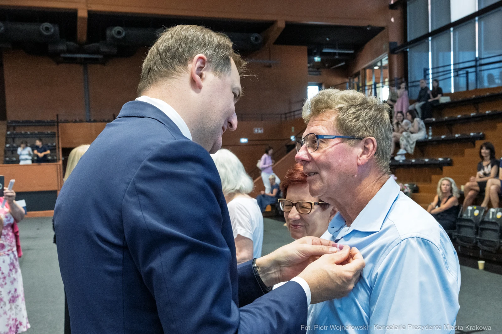 Mężczyzna w garniturze rozmawia z innym mężczyzną w niebieskiej koszuli. W tle widoczni inni uczestnicy wydarzenia.  Autor: Piotr Wojnarowski