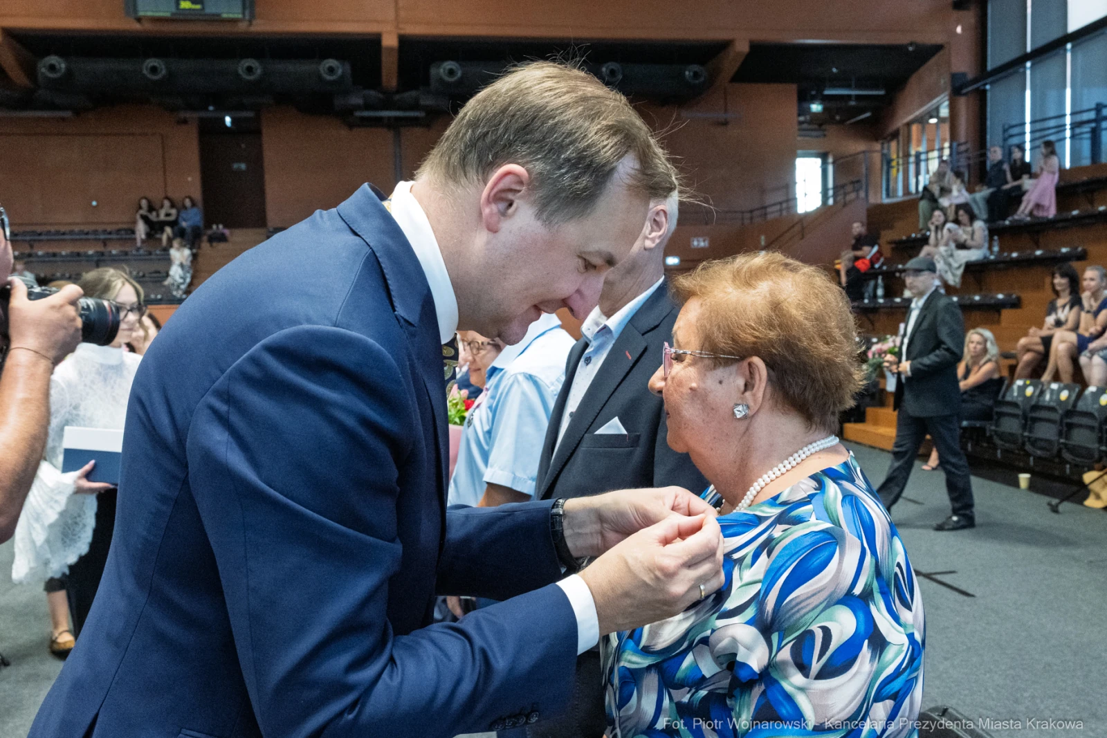 Wręczenie odznaczenia przez mężczyznę starszej kobiecie w uroczystej atmosferze.  Autor: Piotr Wojnarowski