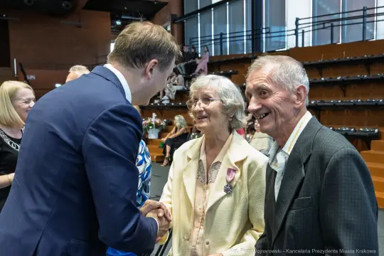 Spotkanie trzech osób, w tym starszej pary, podczas uroczystości.