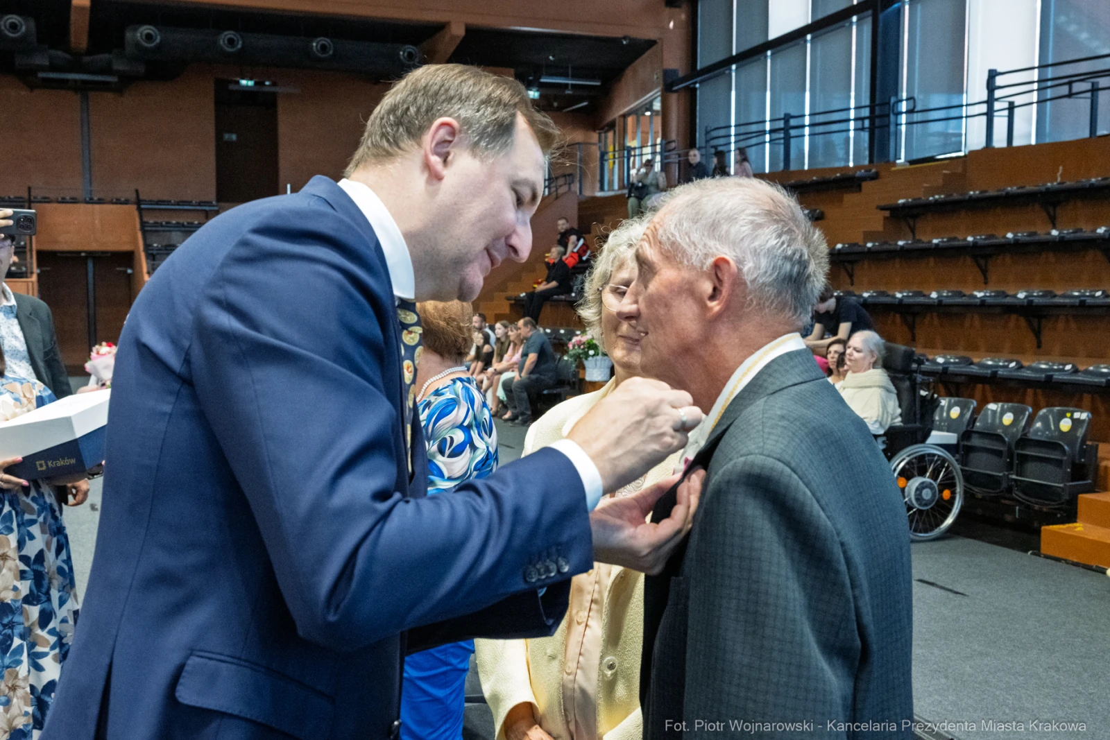 Mężczyzna przypina odznaczenie do marynarki innego mężczyzny w sali pełnej ludzi.  Autor: Piotr Wojnarowski
