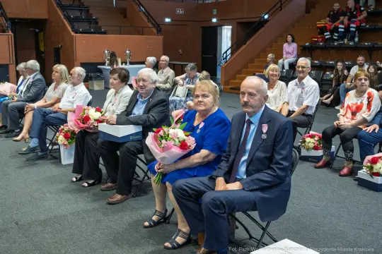 Uczestnicy uroczystości siedzący na widowni, trzymający kwiaty.