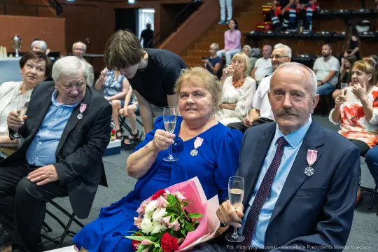Para z kwiatami i szampanem wśród gości na uroczystości.