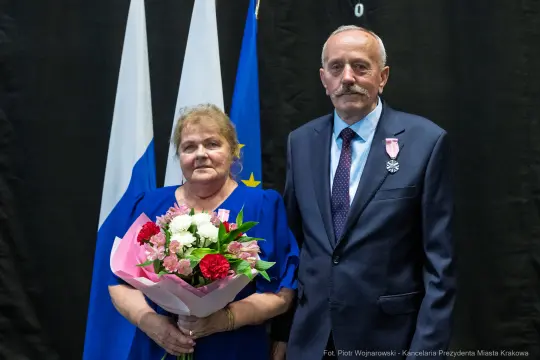 Mężczyzna i kobieta w eleganckich strojach, trzymający bukiet kwiatów, z medalami na piersiach.