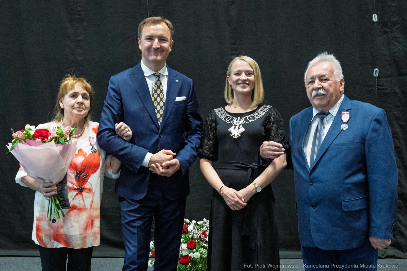 Cztery osoby pozujące razem, jedna z bukietem kwiatów, inne w eleganckich strojach.  Autor: Piotr Wojnarowski
