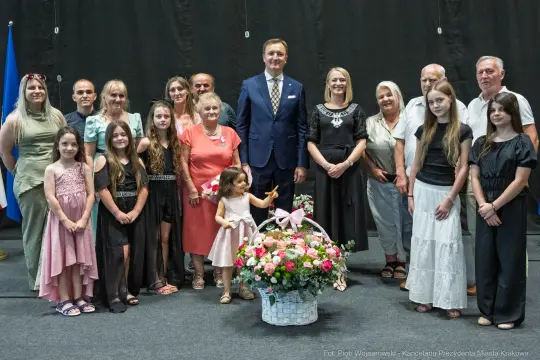 Grupa osób pozujących do zdjęcia z kwiatami na scenie.