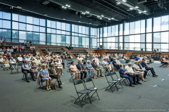 Zgromadzenie ludzi siedzących na krzesłach w dużej sali.