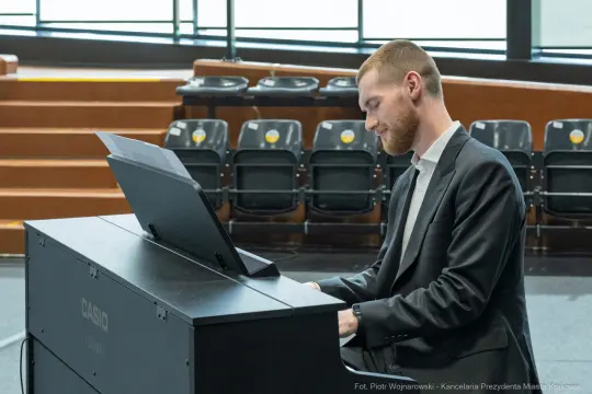 Mężczyzna gra na pianinie w eleganckim stroju.