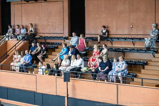 Grupa ludzi siedzących na widowni w sali.