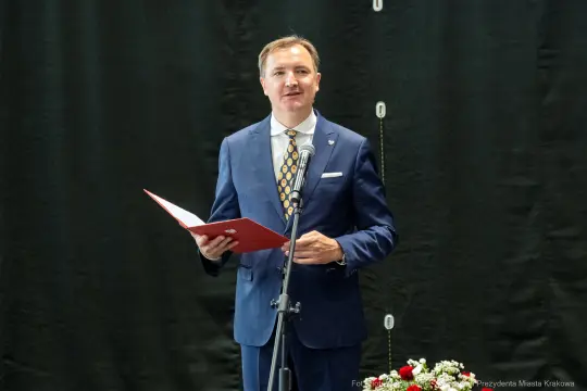 Mężczyzna w garniturze przemawia do mikrofonu, trzymając dokument.