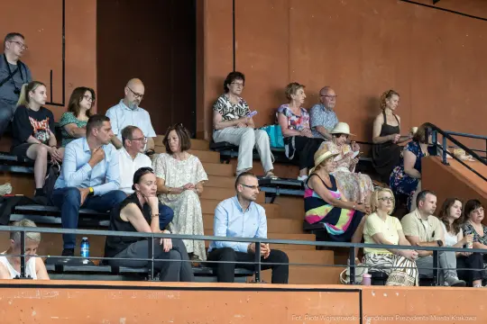Grupa ludzi siedzących na trybunach, różnorodne stroje i postawy.