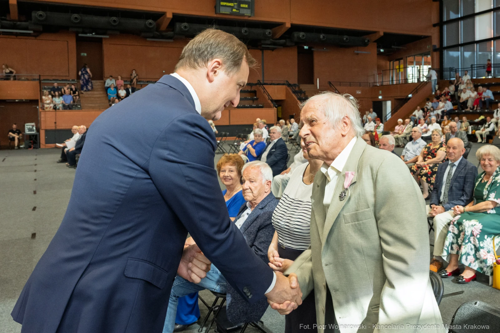 Spotkanie młodszego mężczyzny z starszym, uściski dłoni, w tle publiczność.  Autor: Piotr Wojnarowski