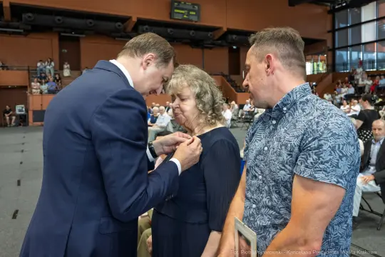 Uroczystość wręczenia odznaczeń, mężczyzna przypina medal kobiecie.