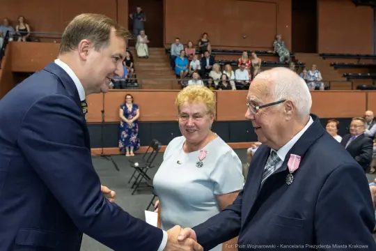Uroczystość wręczenia odznaczeń, mężczyzna w garniturze wita starszego mężczyznę.
