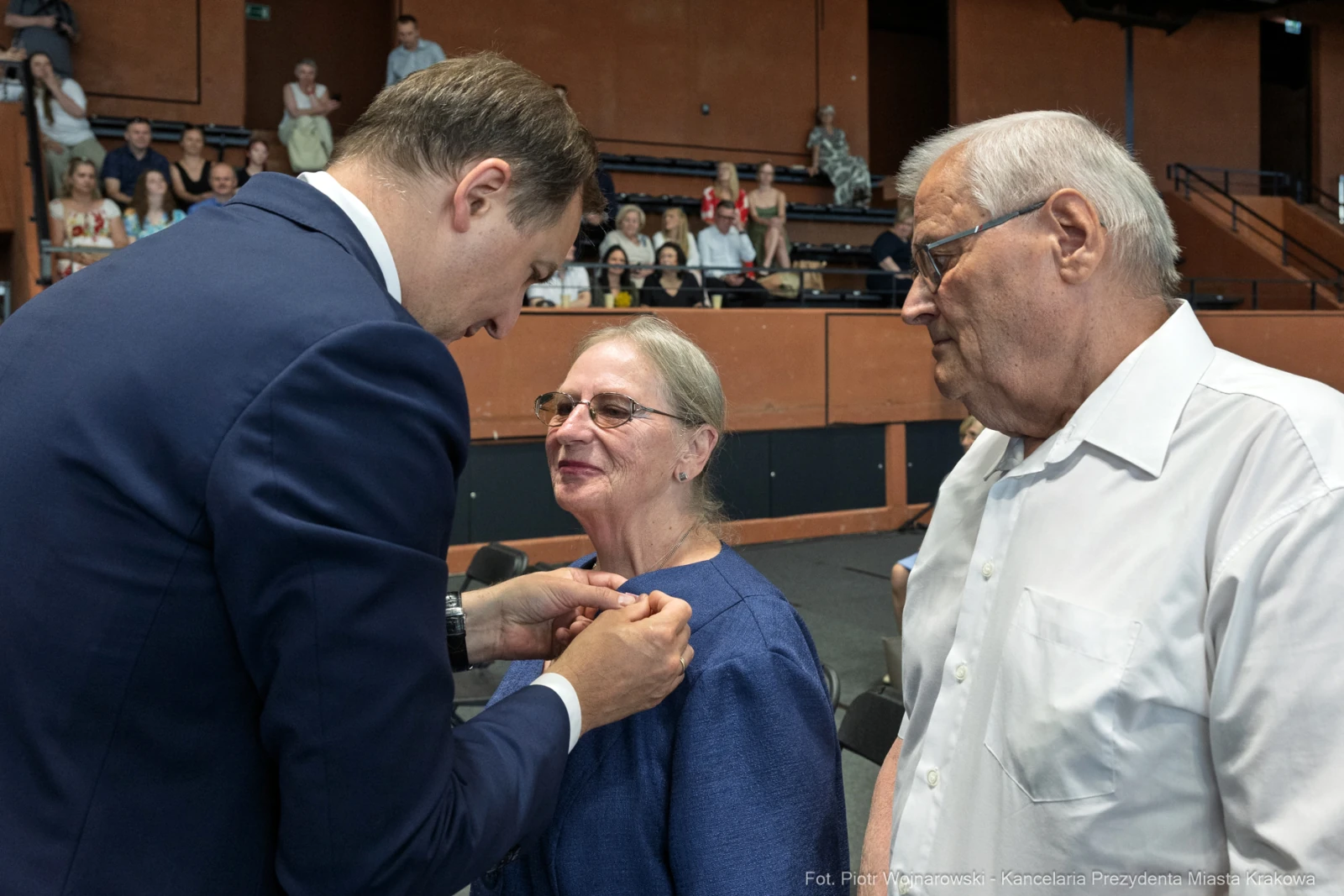 Wręczenie odznaczenia kobiecie przez mężczyznę w obecności starszego mężczyzny.  Autor: Piotr Wojnarowski