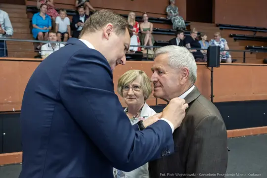 Wręczenie odznaczenia mężczyźnie przez innego mężczyznę, w tle widownia.