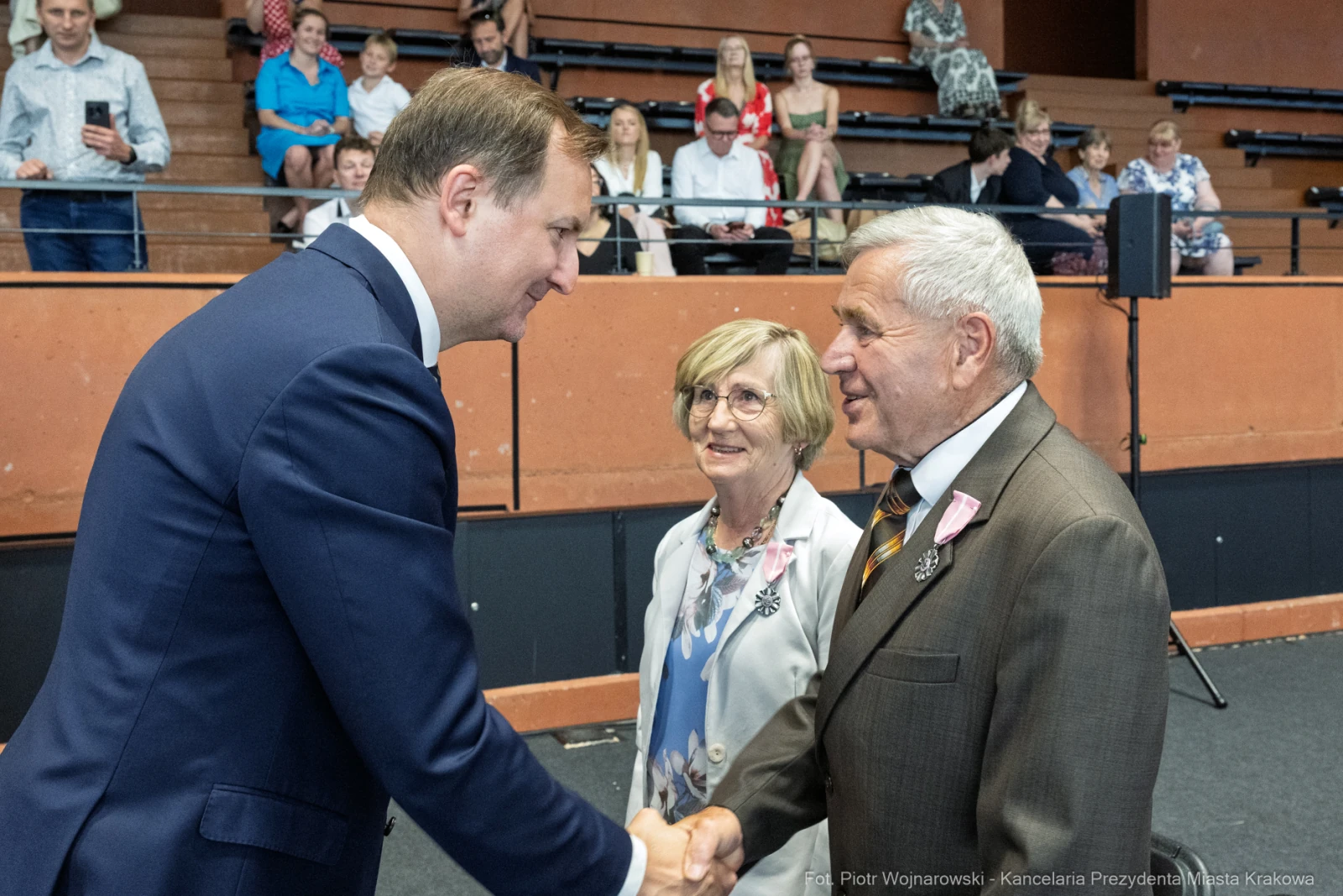 Spotkanie mężczyzny w garniturze z dwoma starszymi osobami, w tle widownia.  Autor: Piotr Wojnarowski