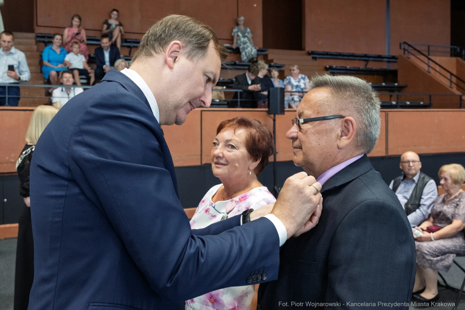 Mężczyzna poprawia krawat innego mężczyzny, obok stoi uśmiechająca się kobieta.  Autor: Piotr Wojnarowski