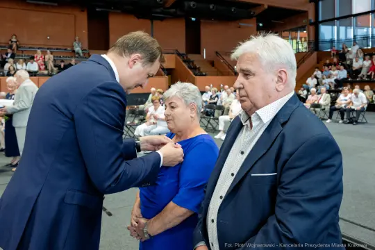Wręczenie odznaczenia kobiecie przez mężczyznę w formalnym otoczeniu.