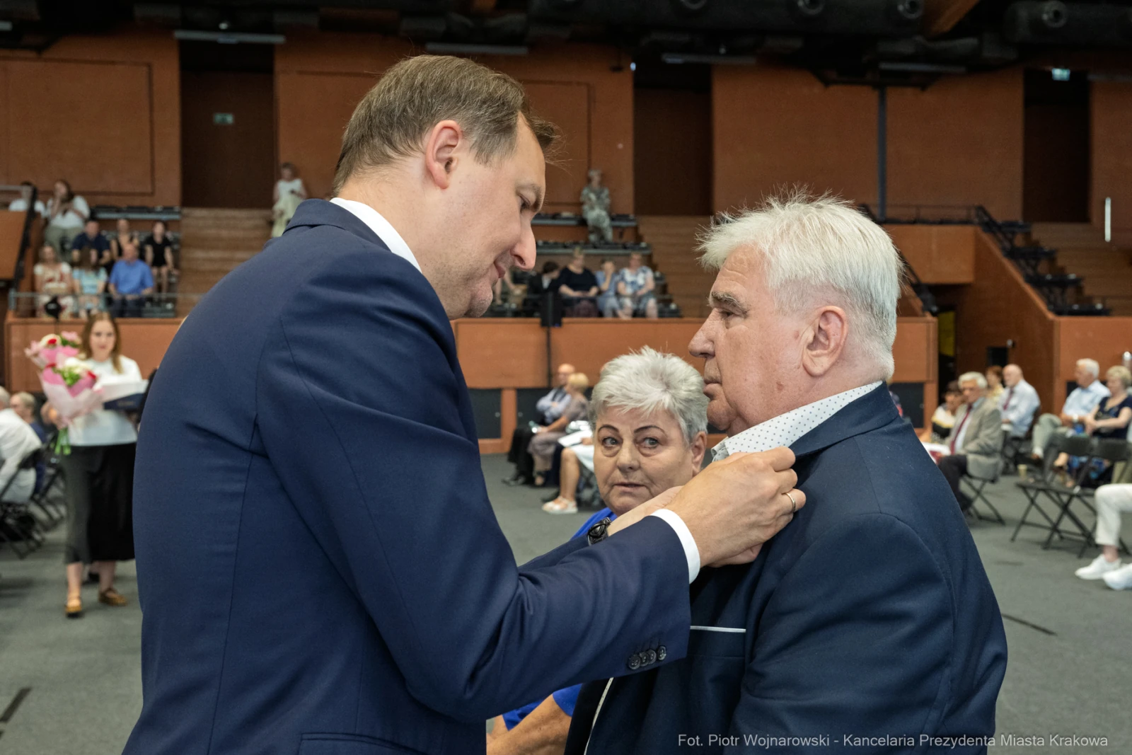 Wręczenie odznaczenia mężczyźnie przez innego mężczyznę w obecności kobiety.  Autor: Piotr Wojnarowski