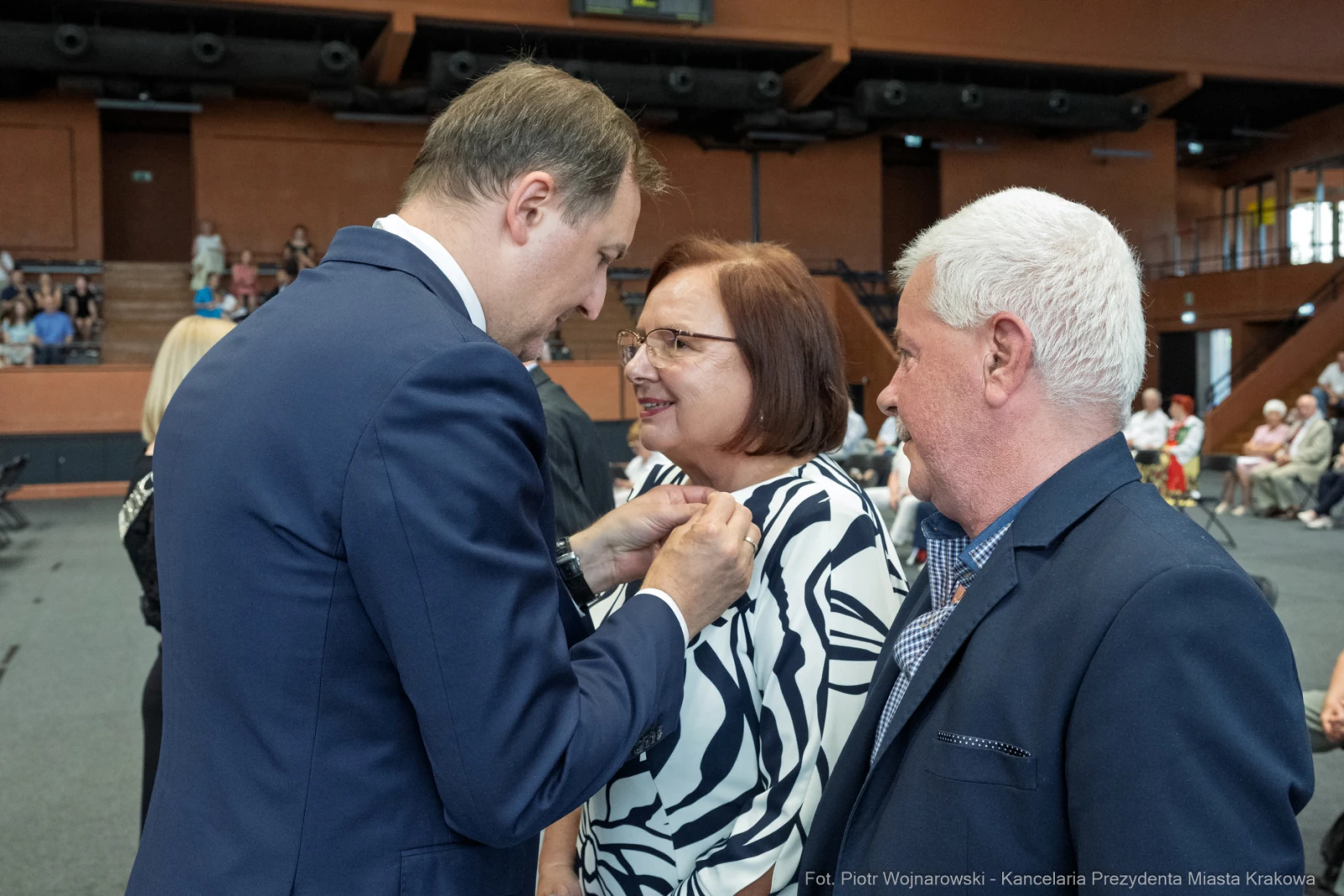Wręczenie odznaczenia przez mężczyznę kobiecie w towarzystwie innego mężczyzny.  Autor: Piotr Wojnarowski
