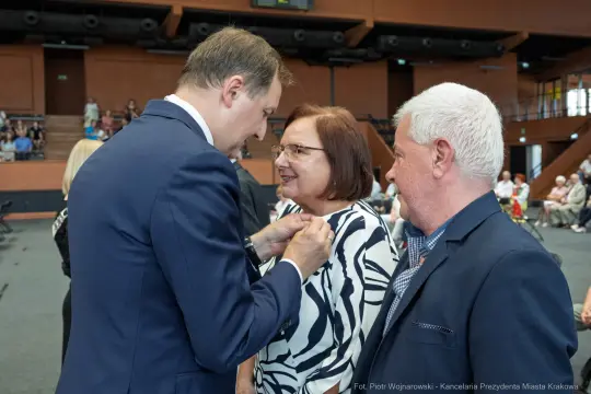 Wręczenie odznaczenia przez mężczyznę kobiecie w towarzystwie innego mężczyzny.