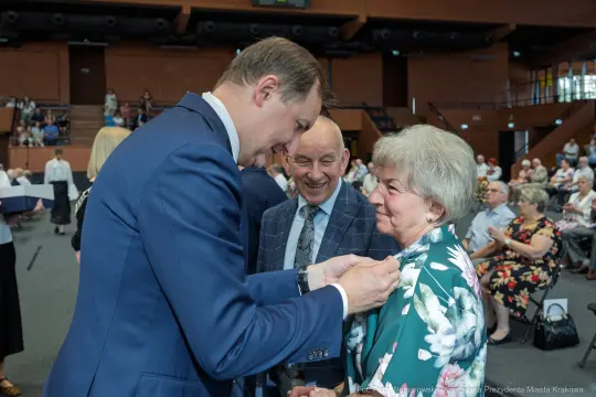 Uroczystość wręczenia odznaczeń, uśmiechnięte twarze, radosna atmosfera.