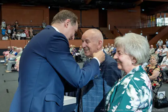 Uroczystość wręczenia odznaczeń, uśmiechnięte twarze jubilatów i gratulacje.