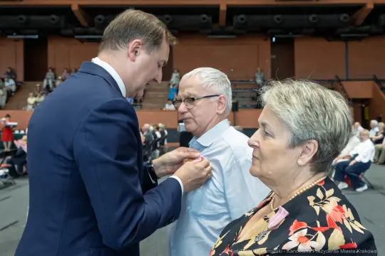 Wręczenie odznaczenia mężczyźnie przez urzędnika w obecności kobiety.