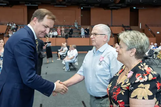 Wręczenie odznaczeń przez mężczyznę w garniturze dwóm starszym osobom.