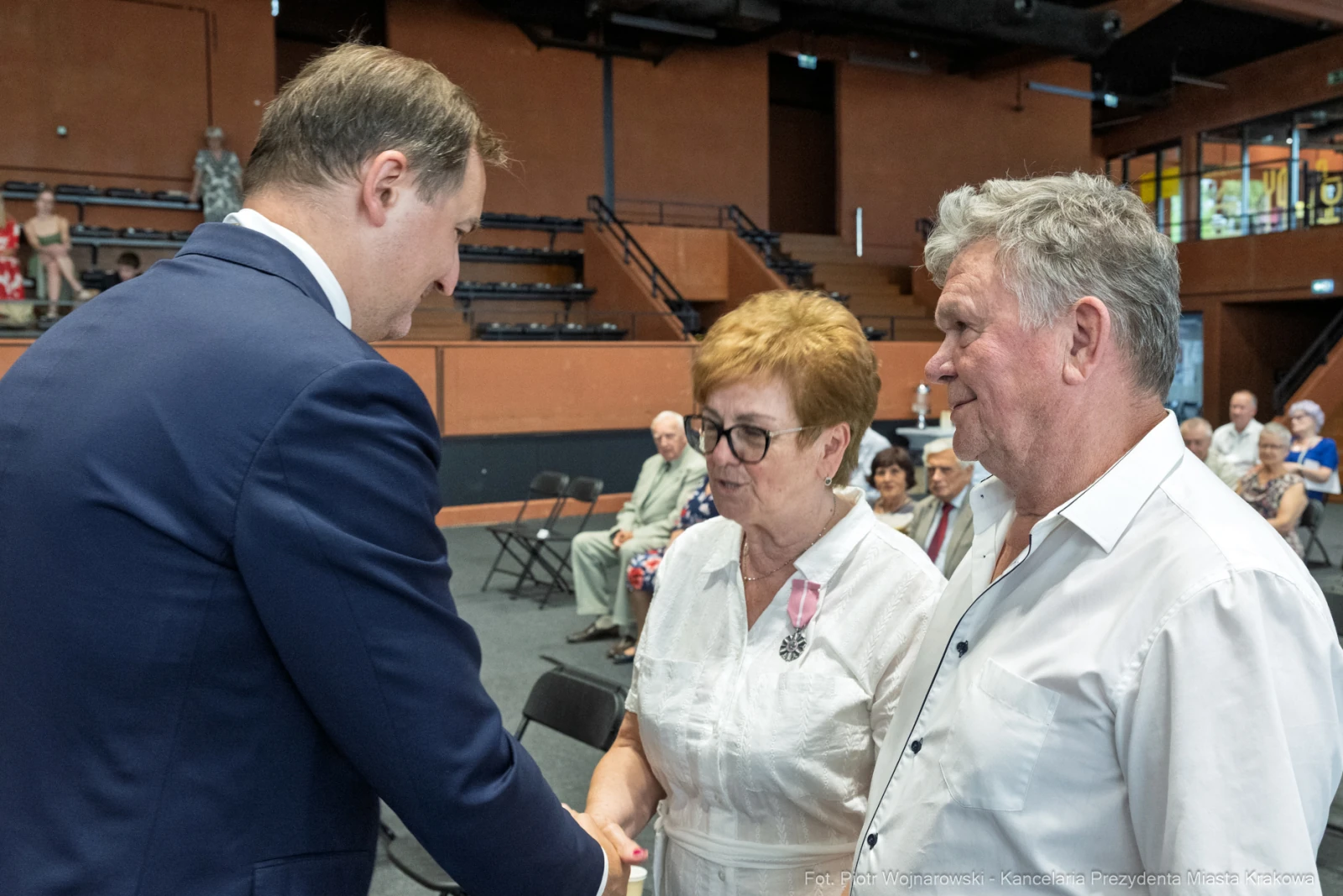 Uroczystość wręczenia odznaczeń, mężczyzna w garniturze wita się z parą starszych osób.  Autor: Piotr Wojnarowski