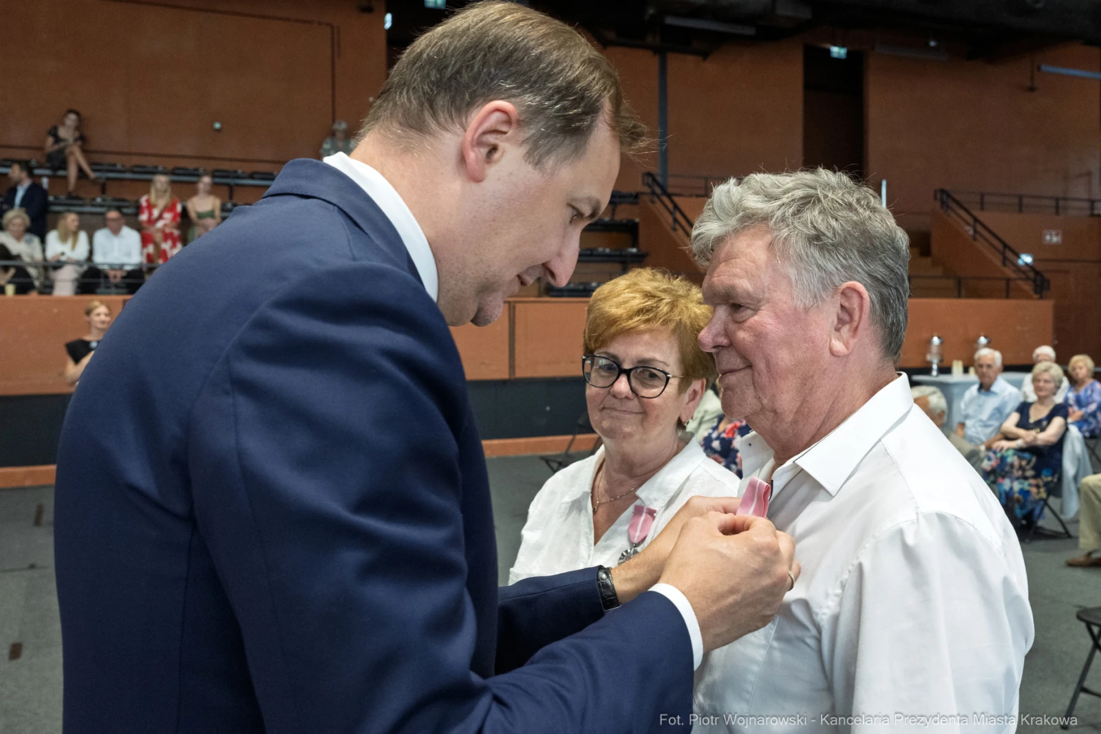 Wręczenie odznaczeń przez mężczyznę starszej parze w sali pełnej widzów.  Autor: Piotr Wojnarowski