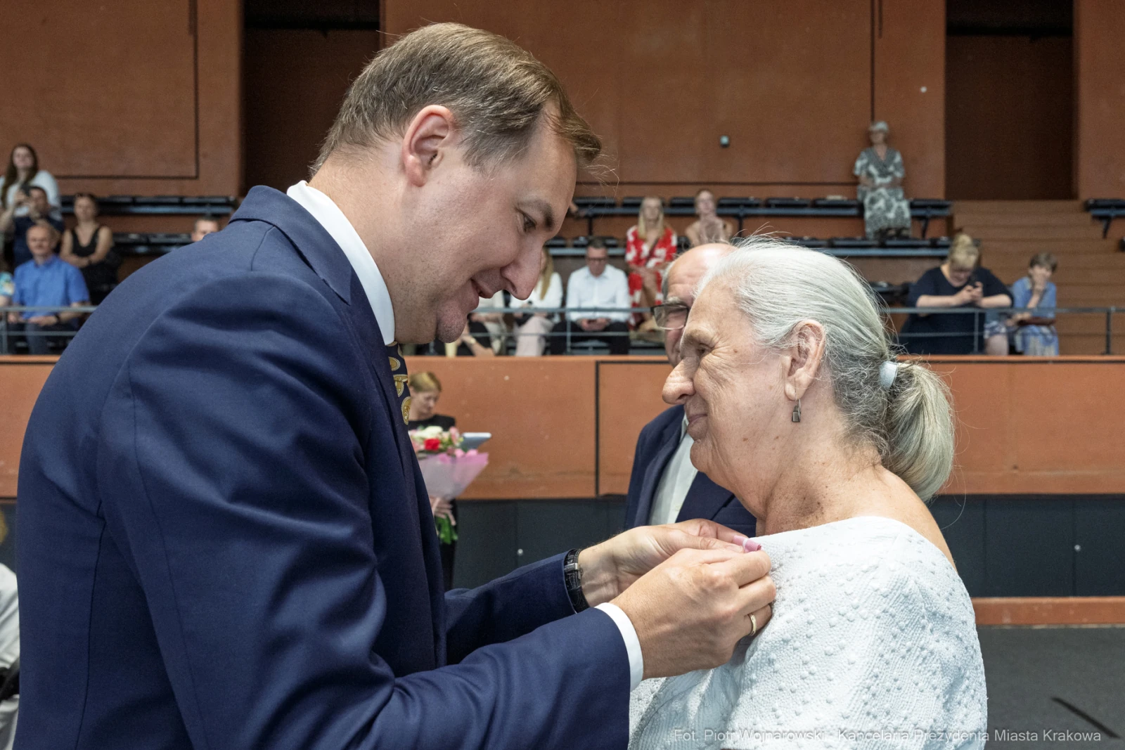 Uroczystość wręczenia odznaczenia starszej kobiecie przez mężczyznę w garniturze.  Autor: Piotr Wojnarowski