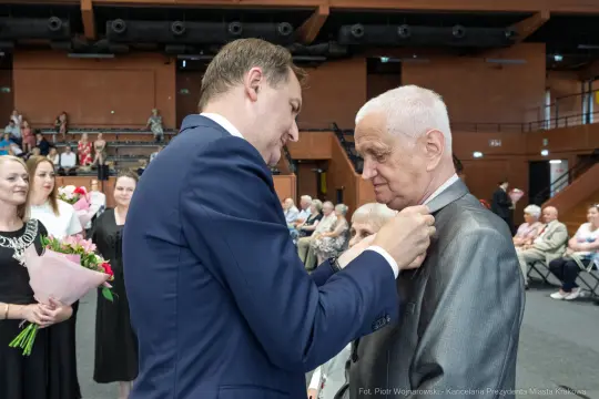 Uroczystość wręczenia odznaczenia mężczyźnie w eleganckim garniturze.