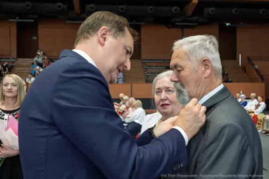 Uroczystość wręczenia odznaczeń, mężczyzna przypina medal do marynarki innego mężczyzny.