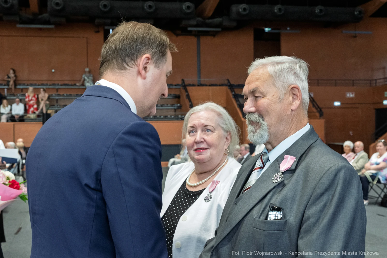 Spotkanie trzech osób, w tym mężczyzny w garniturze i starszej pary, w sali pełnej ludzi.  Autor: Piotr Wojnarowski