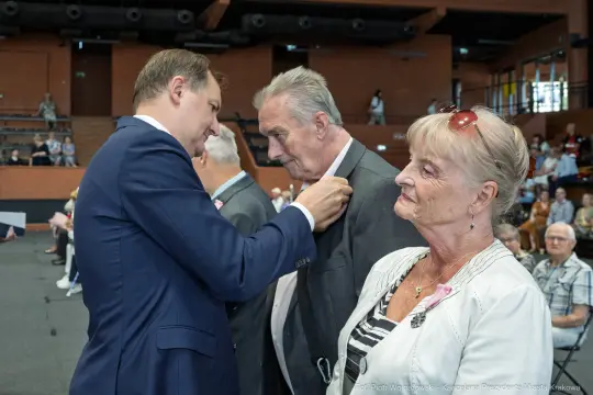 Uroczystość wręczenia odznaczeń, mężczyzna przypina medal do klapy marynarki innego mężczyzny.