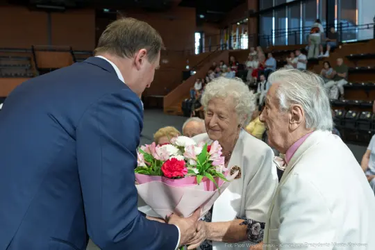 Mężczyzna wręcza bukiet kwiatów starszej parze.