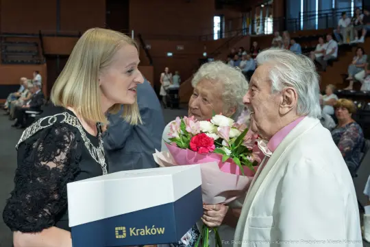Kobieta wręcza kwiaty starszym osobom podczas uroczystości w Krakowie.