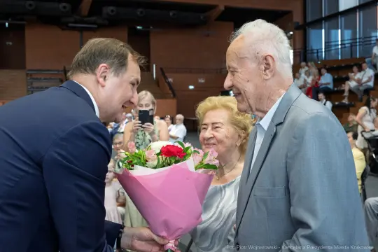 Mężczyzna wręcza bukiet kwiatów starszej parze.