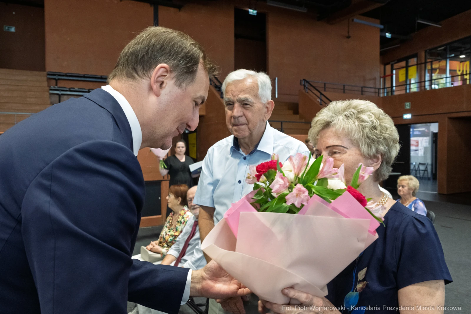 Mężczyzna wręcza bukiet kwiatów starszej kobiecie, w tle inni uczestnicy wydarzenia.  Autor: Piotr Wojnarowski