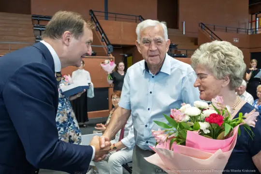 Uroczystość wręczenia kwiatów, uściski dłoni i uśmiechy uczestników.