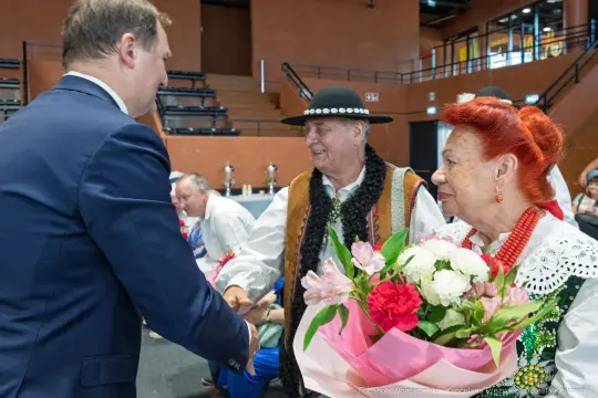 Spotkanie dwóch osób w tradycyjnych strojach ludowych, wręczenie bukietu kwiatów.