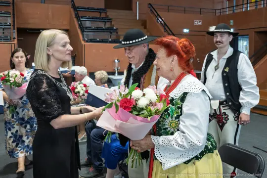 Uroczystość wręczenia kwiatów i gratulacji w tradycyjnych strojach ludowych.