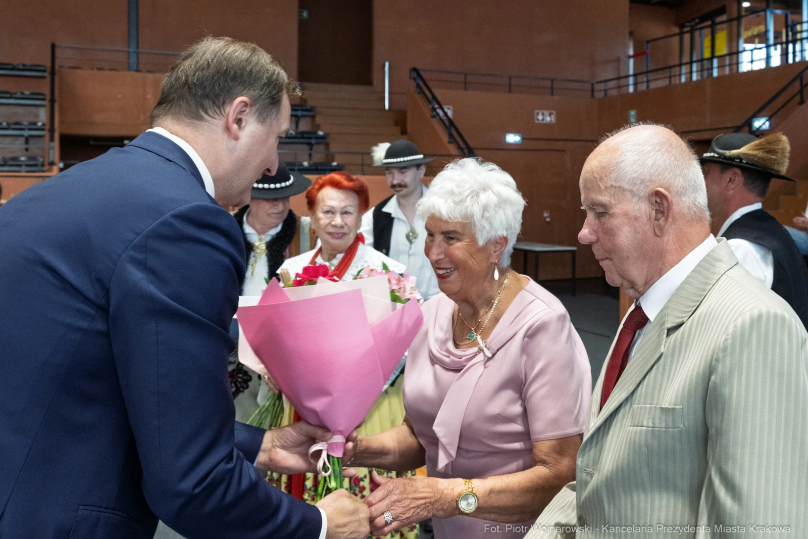 Wręczenie bukietu kwiatów przez mężczyznę starszej kobiecie w towarzystwie innych osób w tradycyjnych strojach.  Autor: Piotr Wojnarowski