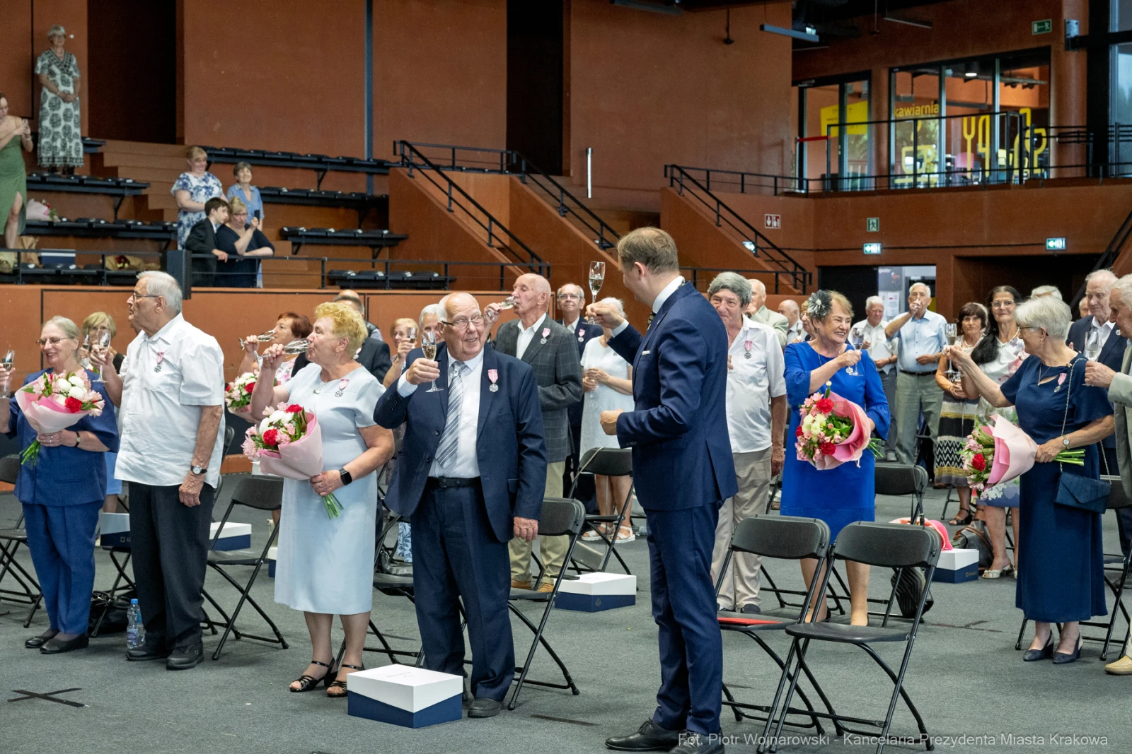Uroczystość z okazji wręczenia odznaczeń, uczestnicy w strojach formalnych z kwiatami.  Autor: Piotr Wojnarowski